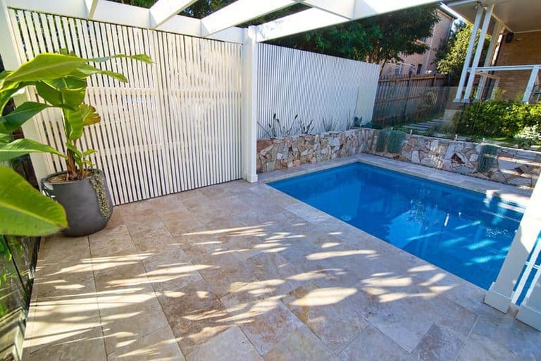 The travertine terrace under the pergola, with the slatted screen and a potted plant beside the pool.