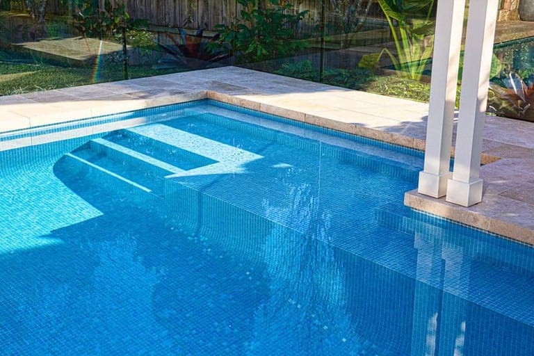 The pool's submerged steps and bench in blue mosaic, with the pergola posts above.