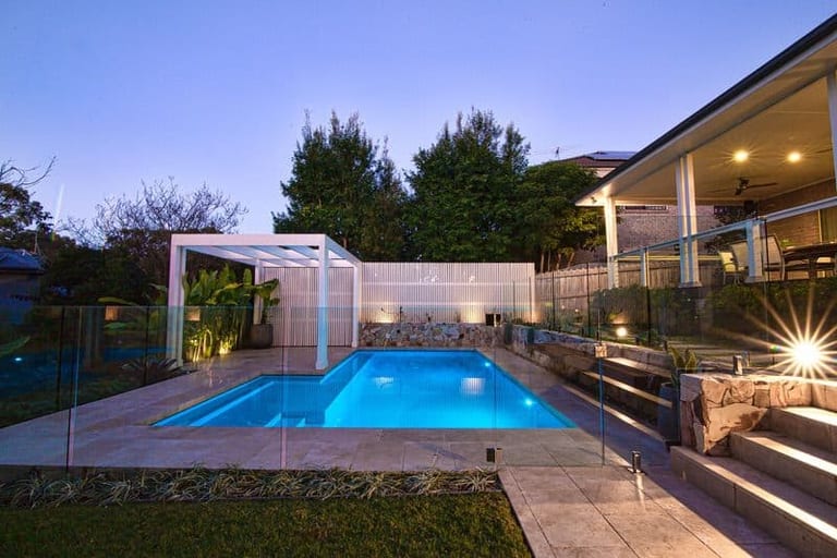 The pool lit at dusk, the house verandah glowing warm and the pergola lit from within.