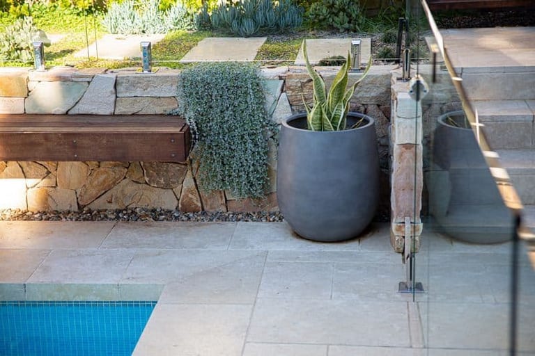 The timber bench and sandstone wall beside the pool, with potted plants and stepping stones above.