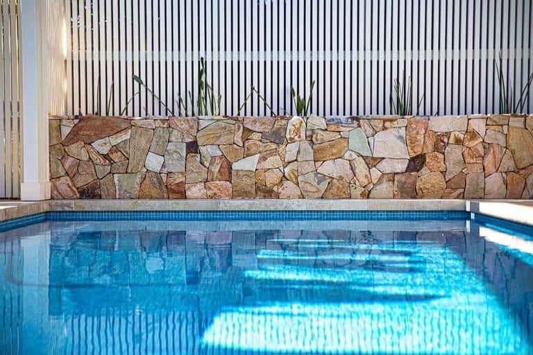 The sandstone wall and reeds reflected in the still blue water of the pool.