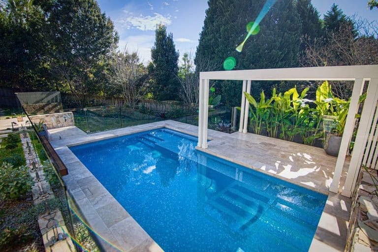 The pool from the lawn corner, conifers and garden beyond, the pergola at right.