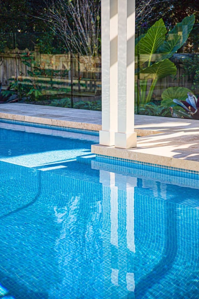 Pergola posts reflected in the pool, with the submerged bench and glass fencing behind.