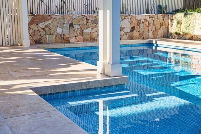 The pool's steps and submerged bench against the sandstone wall, pergola post rising through.