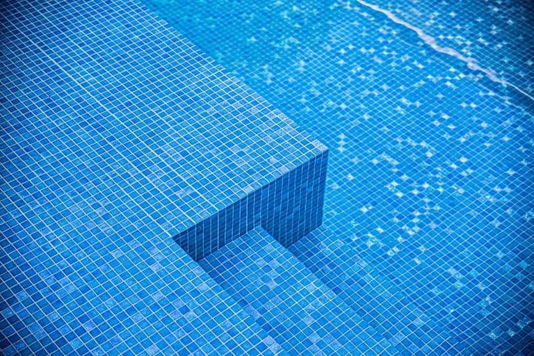The pool's blue mosaic steps and bench seen through clear water.
