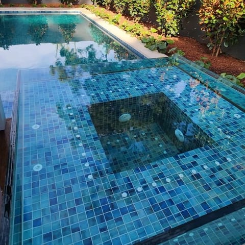 A raised spa finished in blue mosaic tile beside the pool, its jets set into the seat ledges, with garden beds beyond.